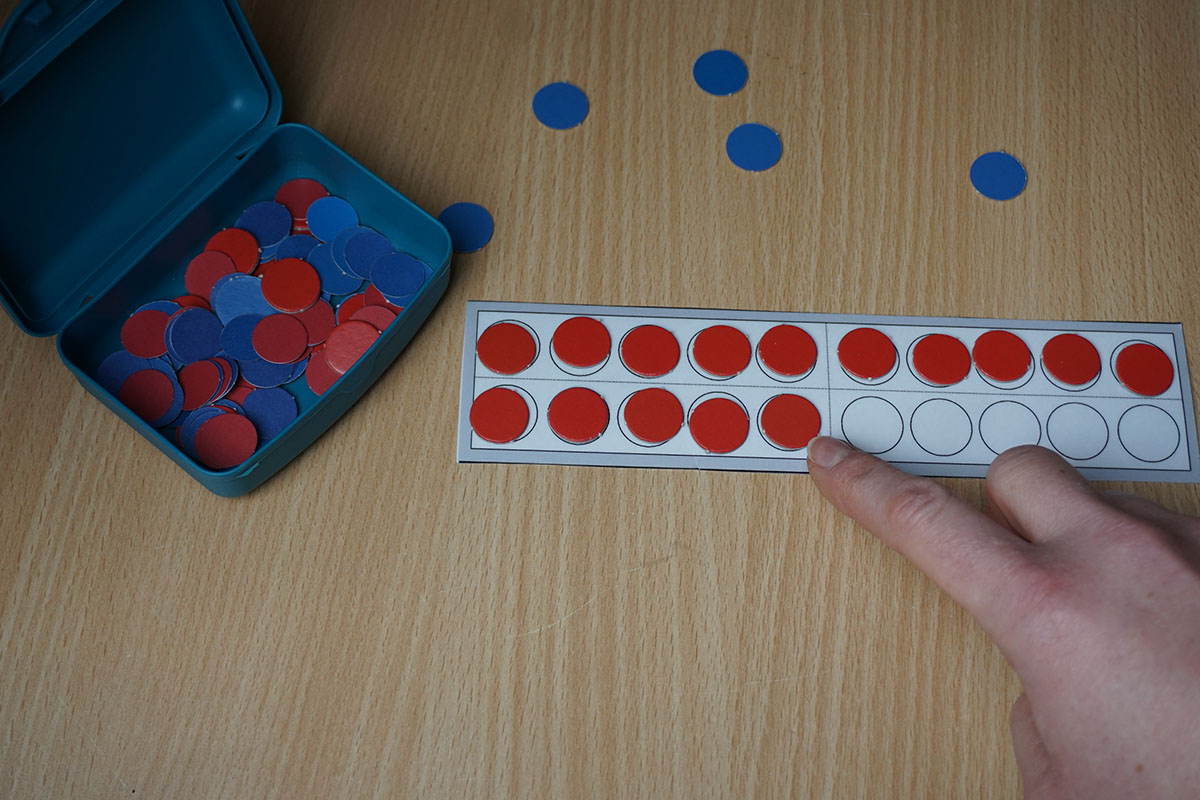 Eine Hand legt 5 rote Plättchen in die zweite Reihe des Zwanzigerfels (insgesamt liegen dort 15).