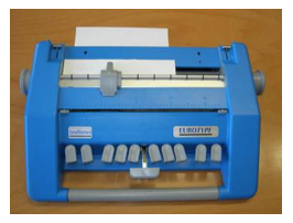 Fotografie einer hellblauen „Eurotype“ Brailleschreibmaschine. Vorne befinden sich 10 kleinere graue Tasten und eine größere, hervorstehende graue Taste. Auf der Oberseite der quaderförmigen Maschine ist ein Schlitz, aus dem das gestanzte Papier herauskommt. 