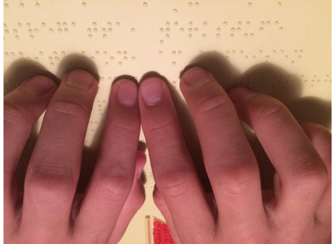 Zwei Hände erfühlen die Braille-Schrift.