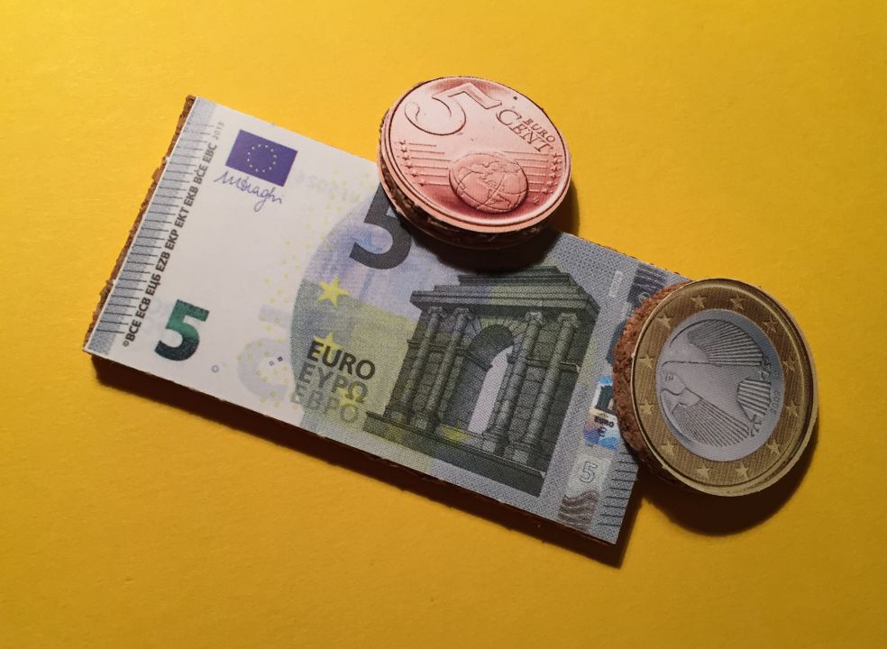 Ein Fünfeuroschein, eine 5-Cent Münze und eine Eineuromünze aus Pappe, darunter Kork.