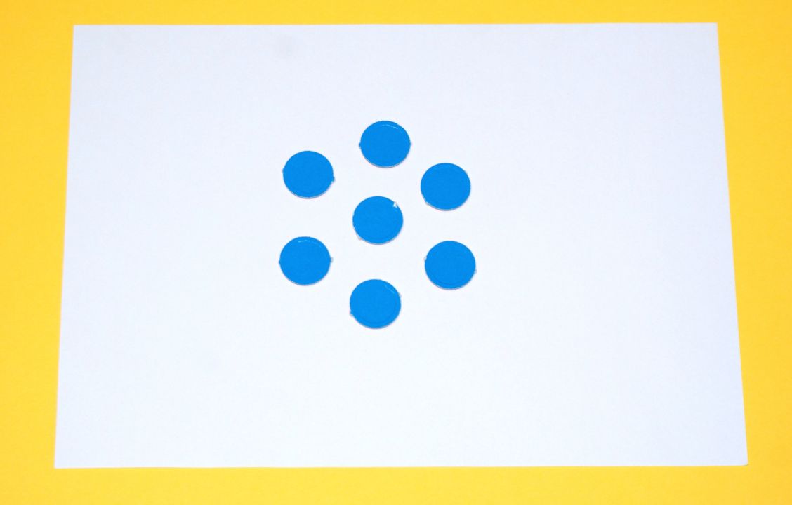 Plättchenanordnung aus 7 blauen Plättchen. Außen: 6 Plättchen in Form eines Sechsecks angeordnet, ein Plättchen in der Mitte.