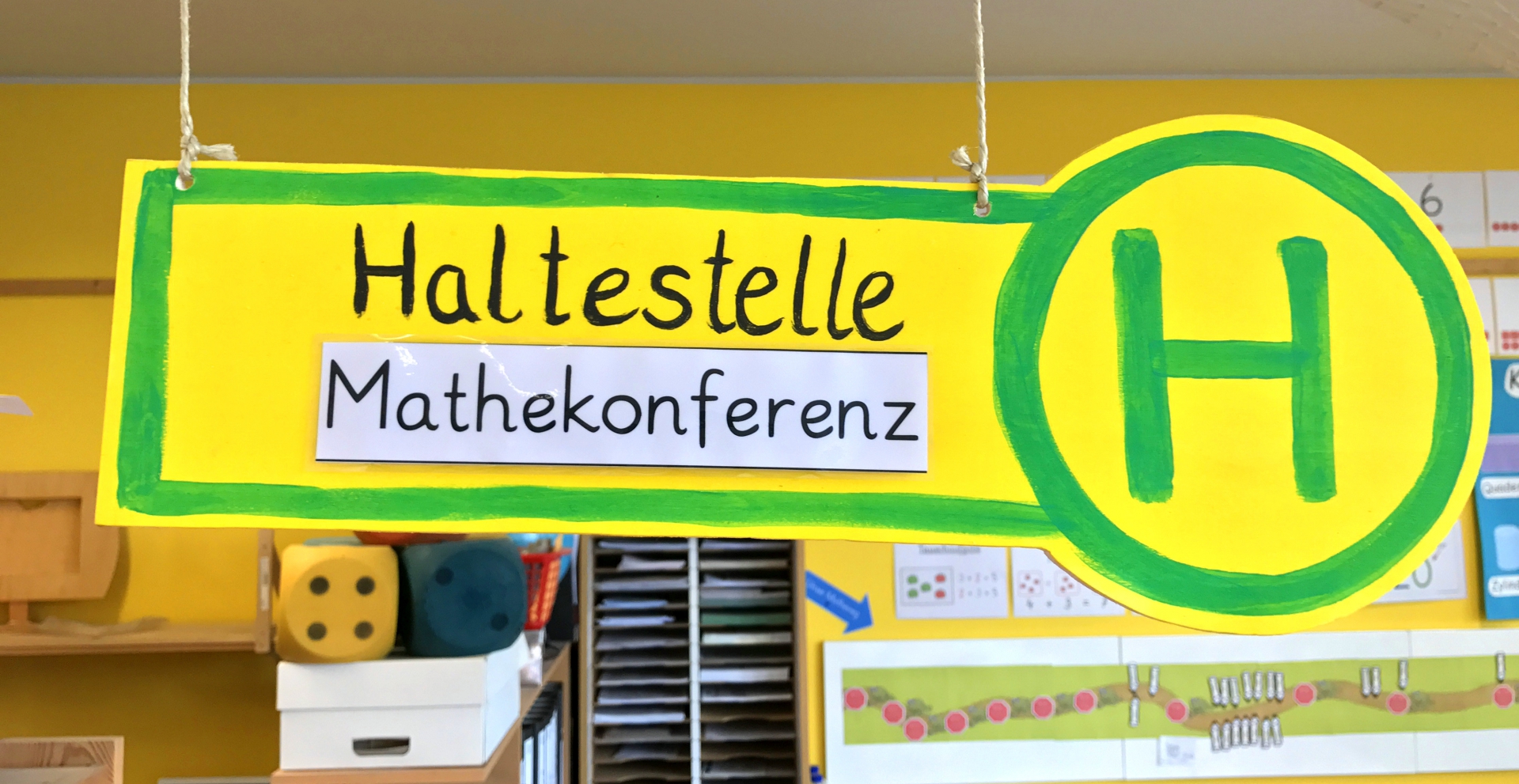 Plakat mit der Aufschrift „Haltestelle Mathekonferenz“ mit Haltestellen-Logo (grünes H auf gelbem Hintergrund).
